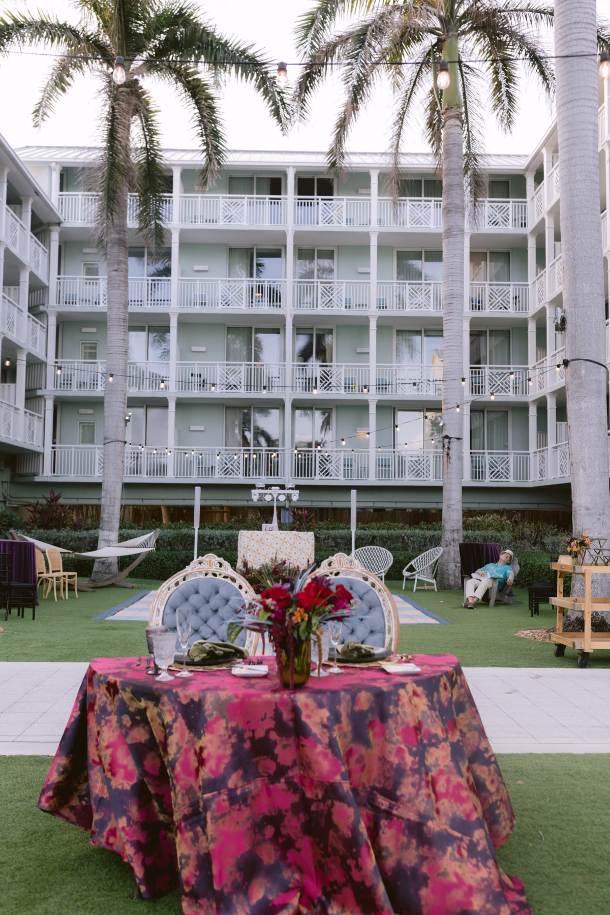 Jewel tone wedding reception table with vibrant floral centerpiece by Arms of Persephone at Casa Marina Key West with palm trees and resort balconies in background