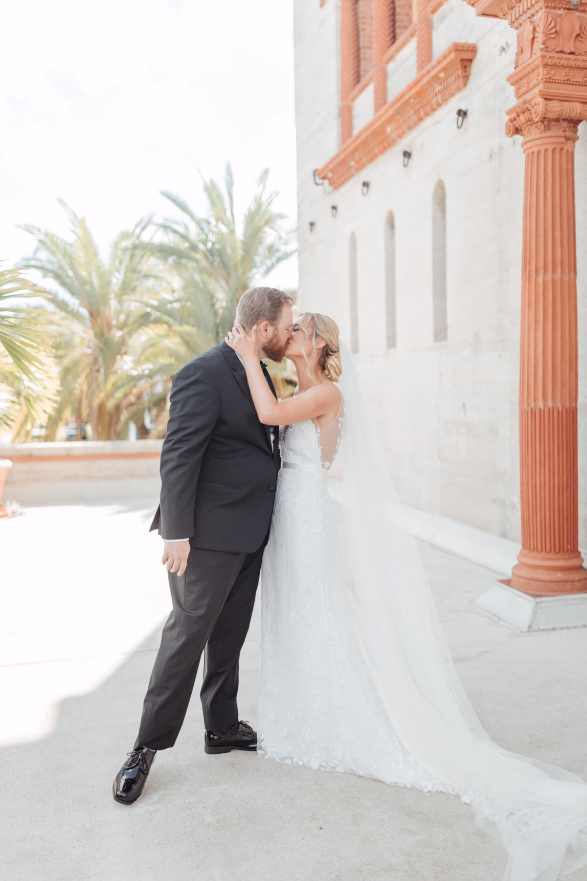 Bride and groom sharing romantic moment at historic Lightner Museum wedding with classical architecture and palm trees, planned by Coastal Celebrations