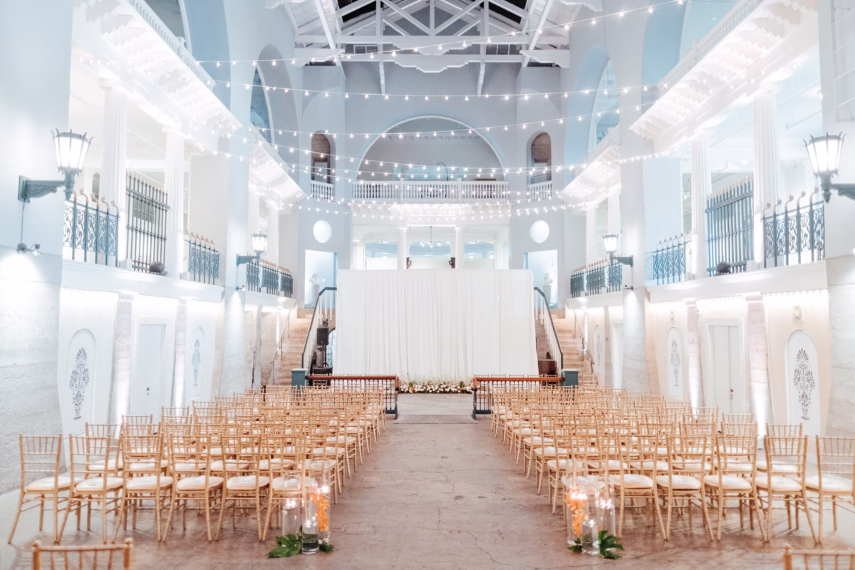 Historic wedding ceremony at The Lightner Museum with gold chiavari chairs and string lights planned by Coastal Celebrations with florals by Aime Peterson Flowers