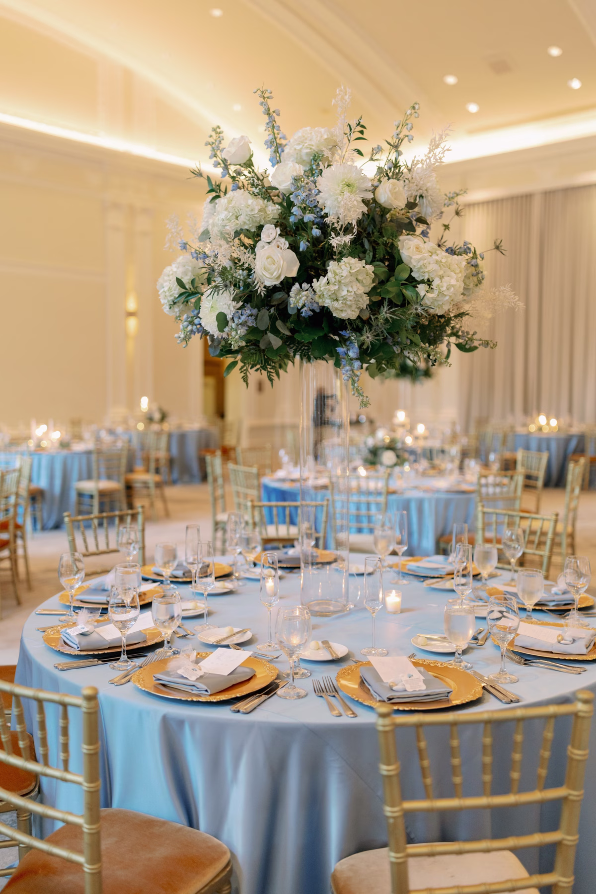 Elegant wedding reception tablescape with tall floral centerpiece by Lemon Drops Weddings and Events at The Vinoy St. Petersburg featuring blue linens and gold chiavari chairs