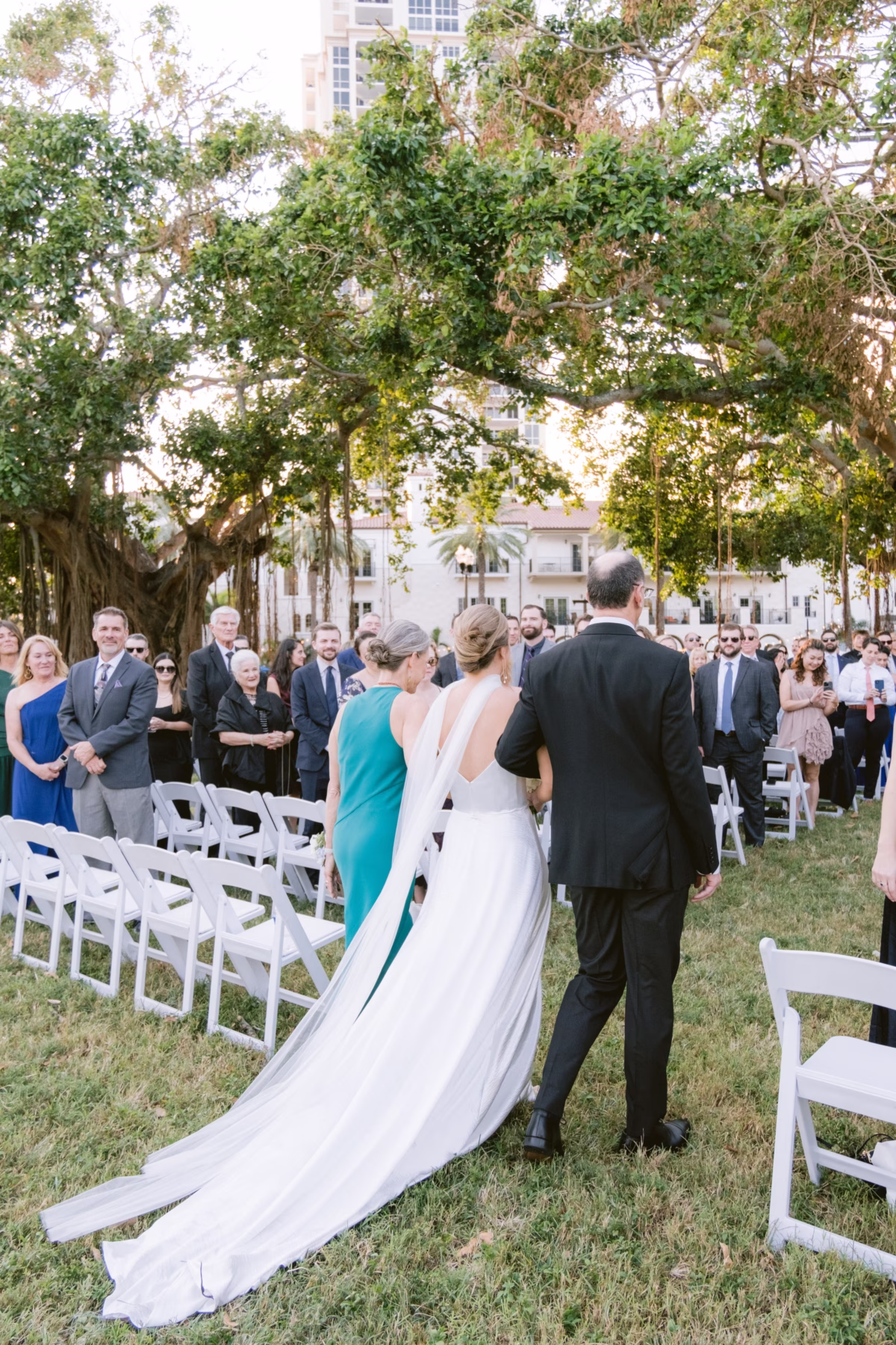 Bride walking down the aisle with her father at an outdoor wedding ceremony under a large banyan tree at Nancy Cotto Events venue in St. Petersburg