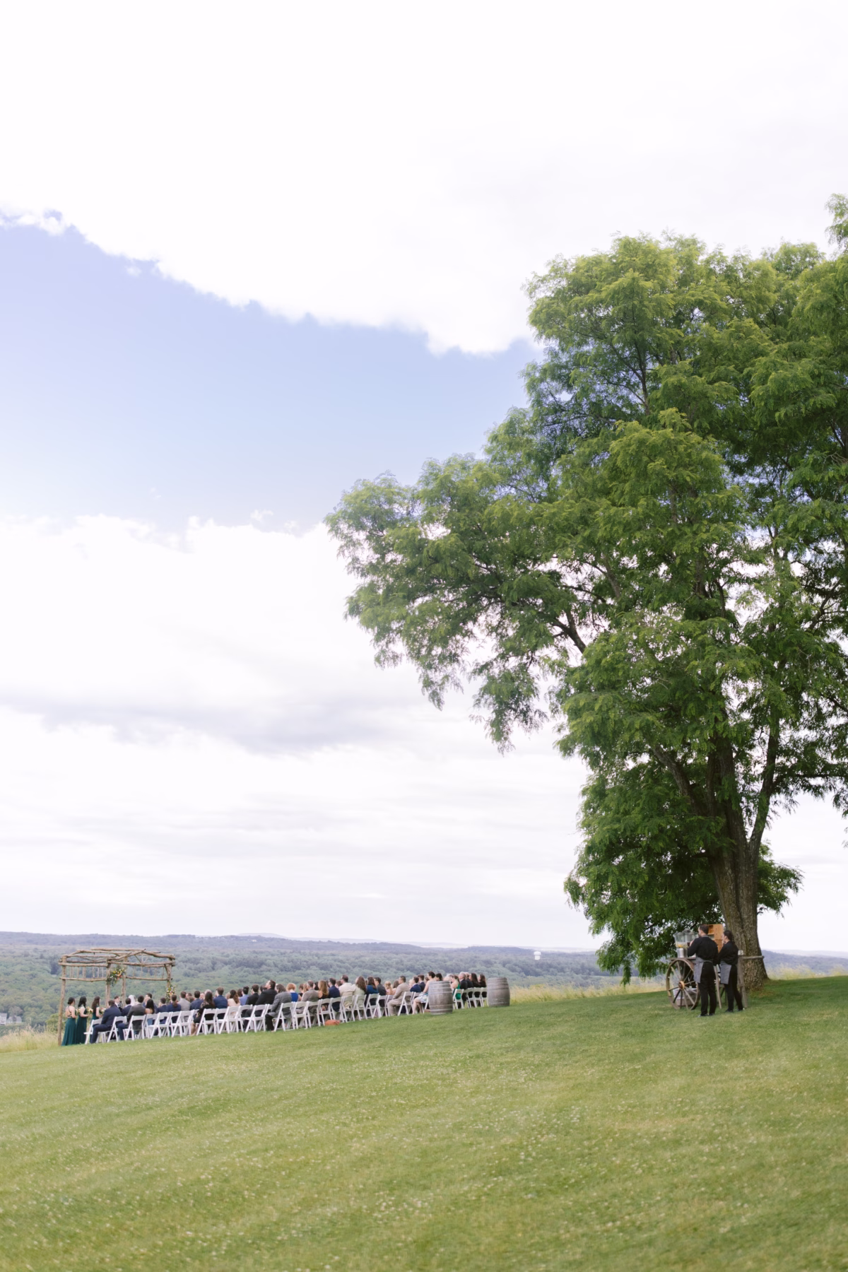 Outdoor wedding ceremony setup with guests seated on lawn under large tree at Red Maple Vineyard photographed by Tampa Bay wedding photographer Ashley Izquierdo