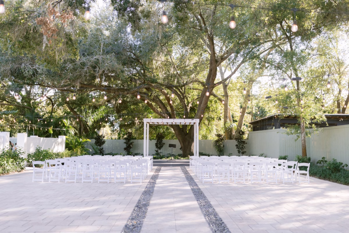 Elegant outdoor wedding ceremony setup with white chairs and modern arch at Soire Estate in Tampa