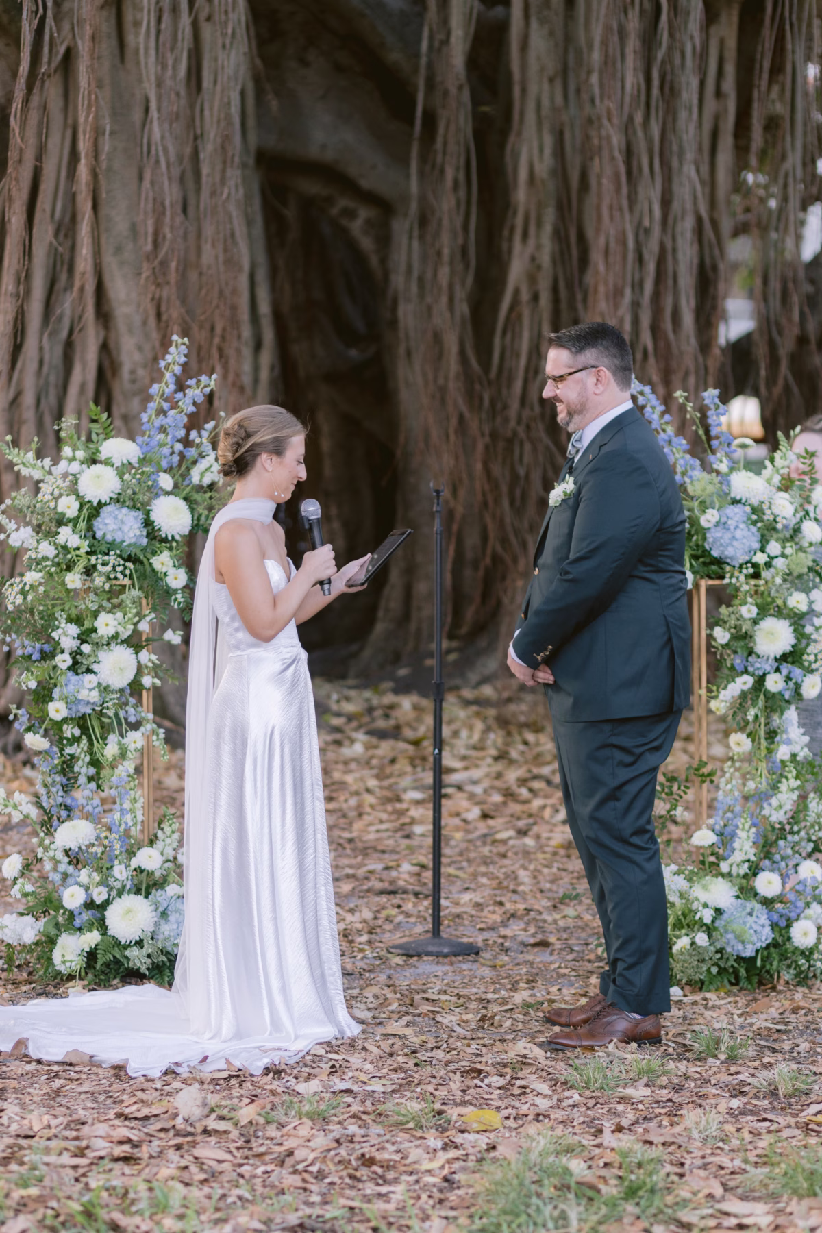 Bride reading vows to groom during outdoor wedding ceremony with blue and white floral arrangements by Wonderland Floral Art at Nancy Cotto Events venue in St. Petersburg