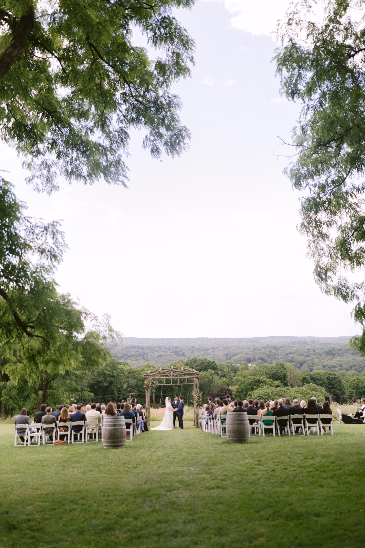 Outdoor wedding ceremony at Red Maple Vineyard with rustic wooden arbor and floral arrangements by Cherry Brandy Designs overlooking rolling vineyard hills