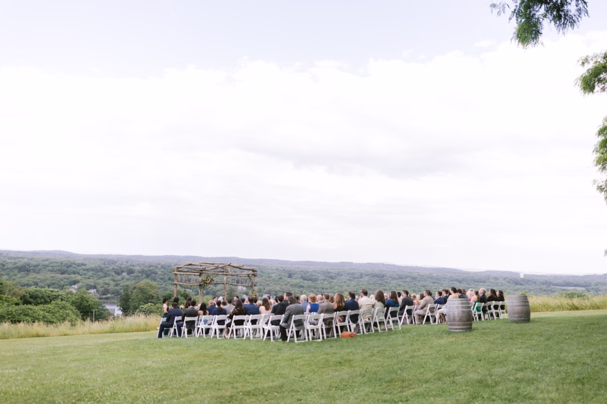 Outdoor wedding ceremony at Red Maple Vineyard with guests seated on lawn facing rustic wooden altar overlooking rolling hills and vineyard landscape