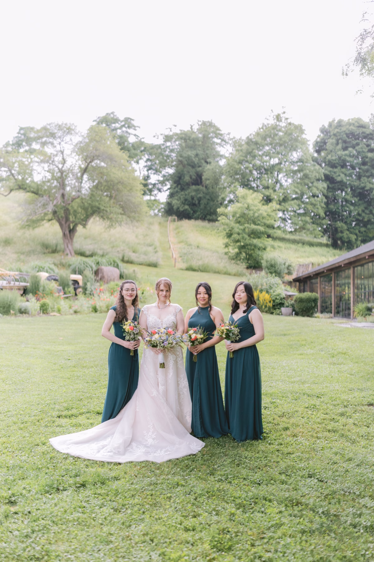Bride in Maggie Sottero gown with bridesmaids in forest green dresses holding Cherry Brandy Designs bouquets at Red Maple Vineyard wedding