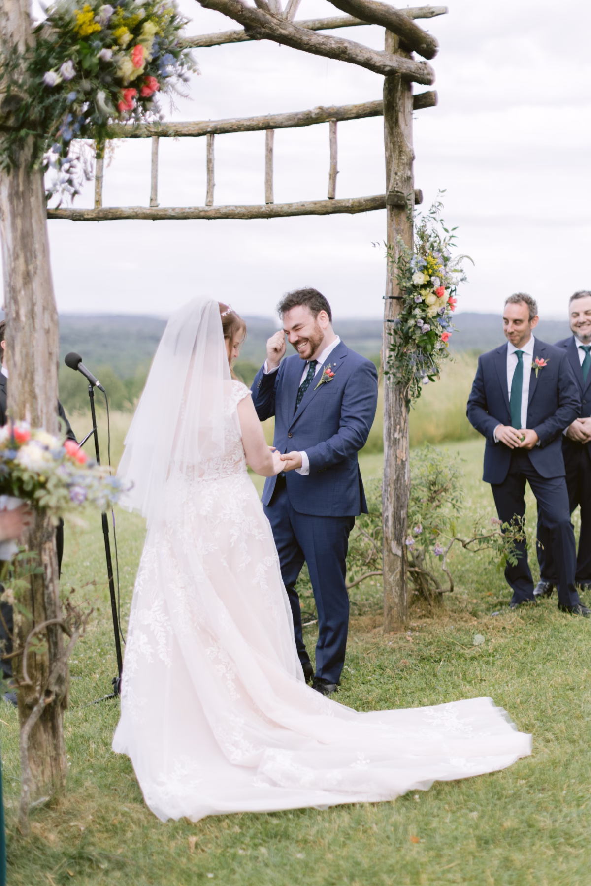 Outdoor wedding ceremony at Red Maple Vineyard with rustic wooden arch decorated by Cherry Brandy Designs florals as bride and groom exchange vows