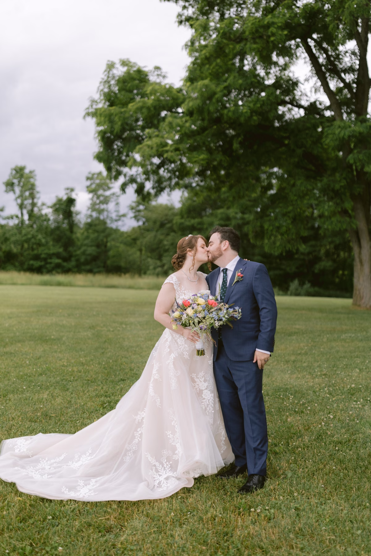 Bride and groom share intimate kiss holding wildflower bouquet by Cherry Brandy Designs at Red Maple Vineyard wedding photographed by Ashley Izquierdo Photography