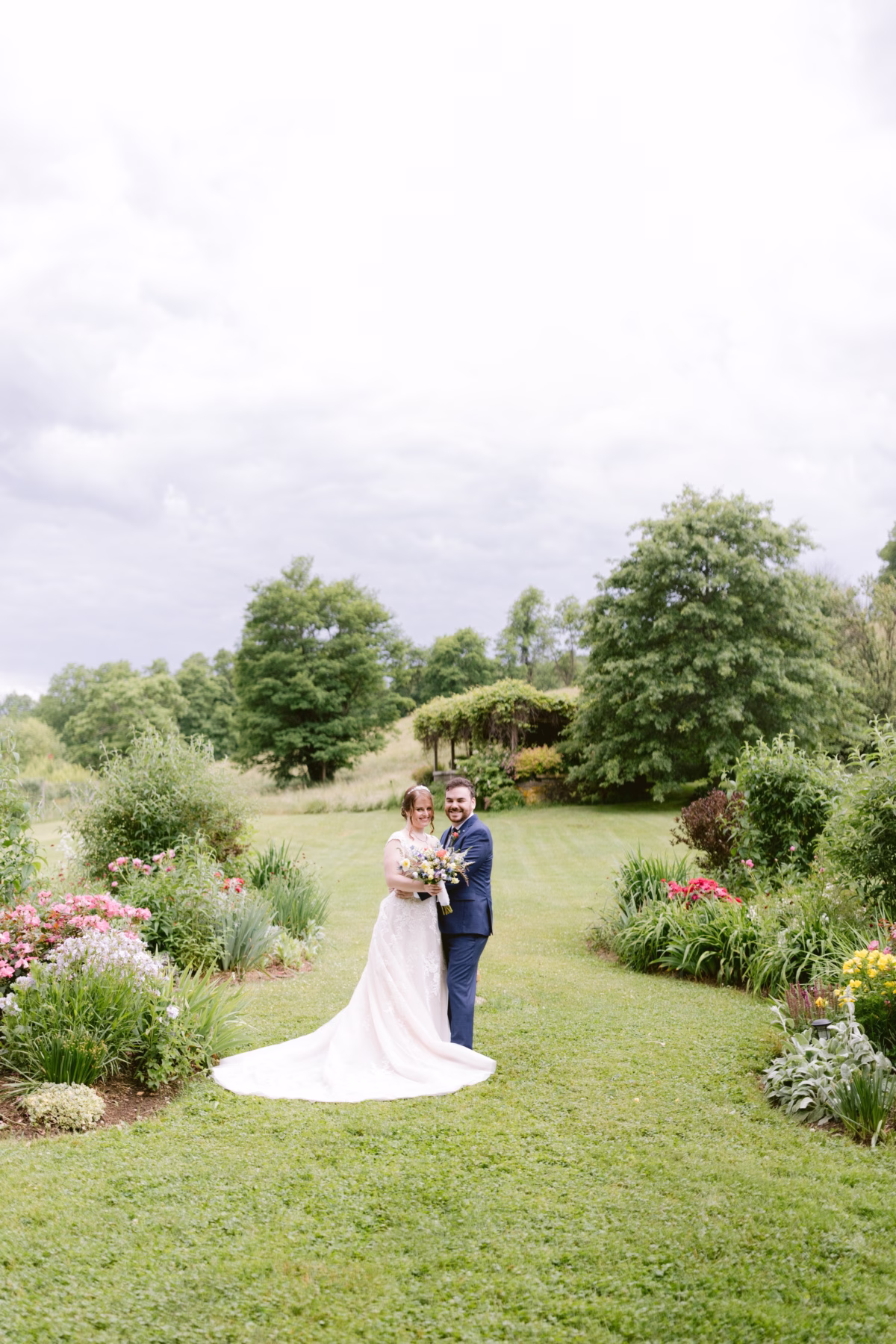 Bride and groom embrace in garden setting with wildflower arrangements by Cherry Brandy Designs at Red Maple Vineyard wedding photographed by Ashley Izquierdo Photography