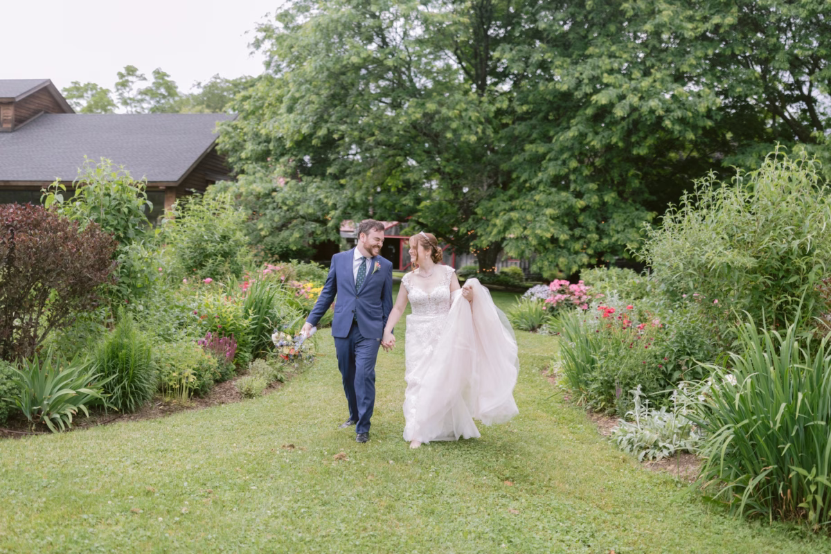 Bride and groom walking hand in hand through lush gardens at Red Maple Vineyard wedding with floral arrangements by Cherry Brandy Designs