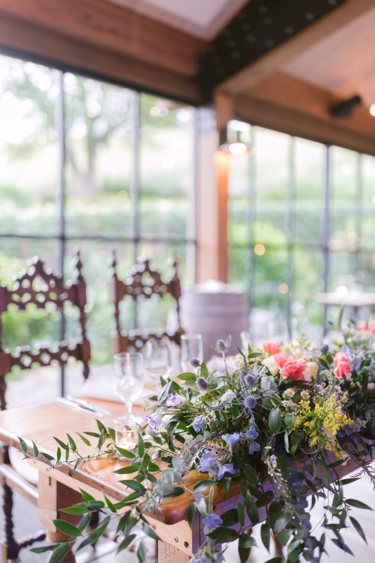 Wildflower wedding centerpiece by Cherry Brandy Designs featuring coral roses and blue thistles on rustic wooden table at Red Maple Vineyard reception