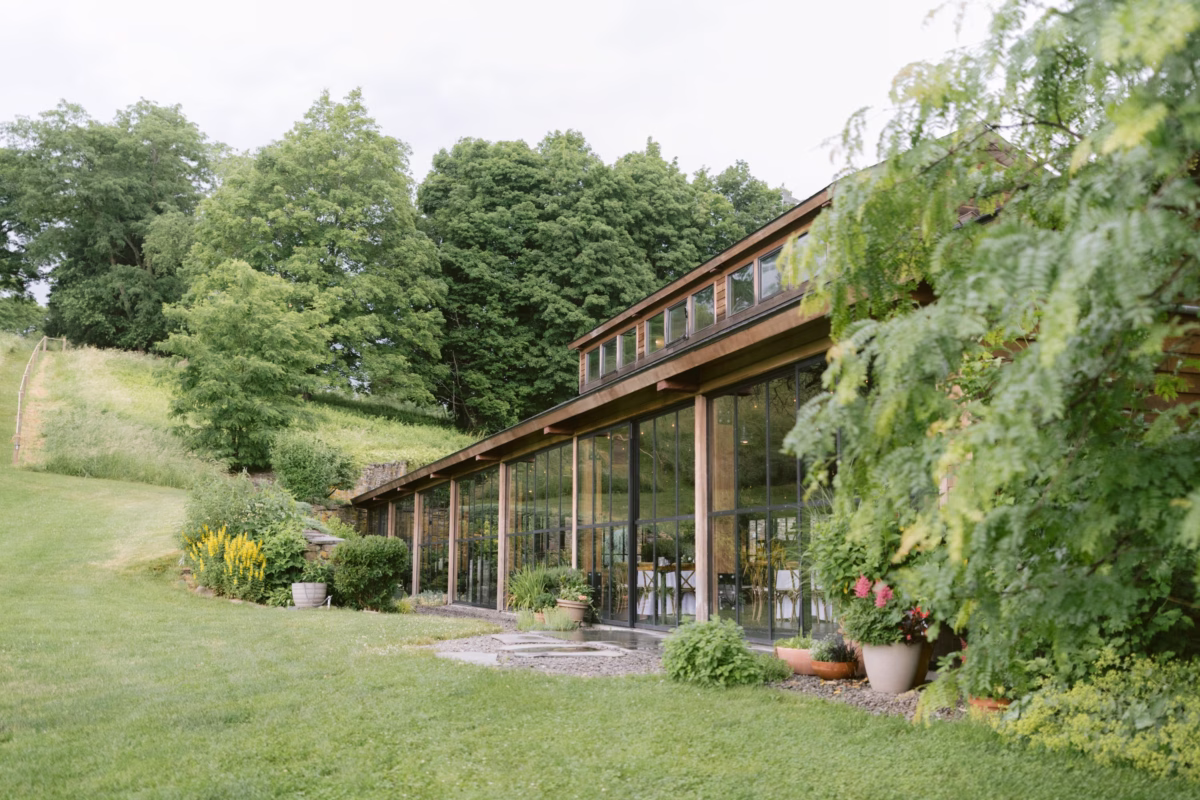 Red Maple Vineyard wedding venue exterior featuring modern glass building with wooden frames surrounded by lush greenery and rolling hills