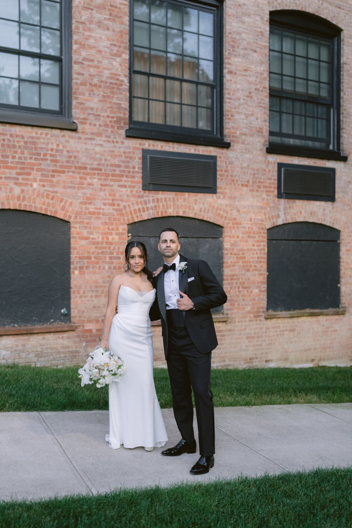 Elegant bride and groom portrait at The Roundhouse Beacon featuring white floral bouquet by Maky The Diva Flowers against historic brick building