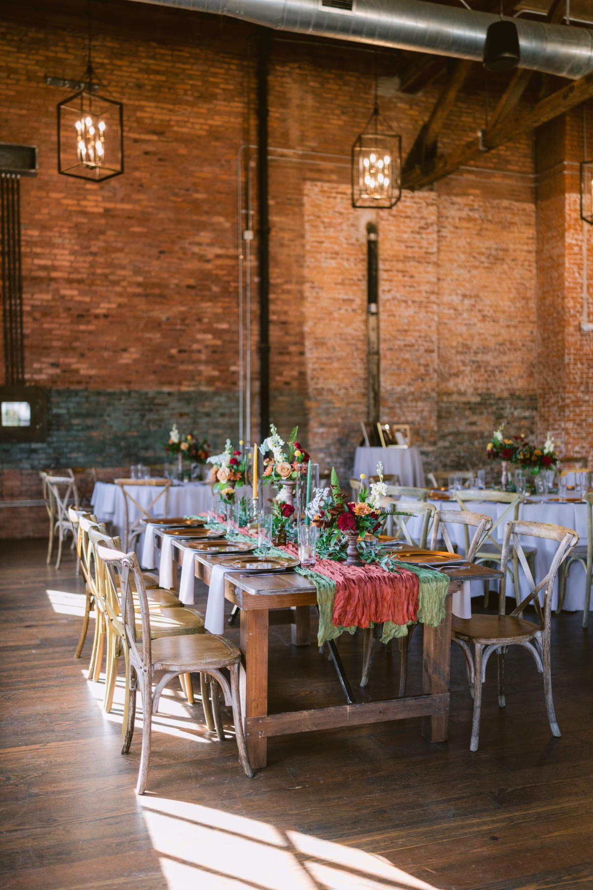 Rustic wedding reception tables with colorful floral centerpieces by Events in Bloom at Armature Works Tampa featuring exposed brick walls and industrial lighting