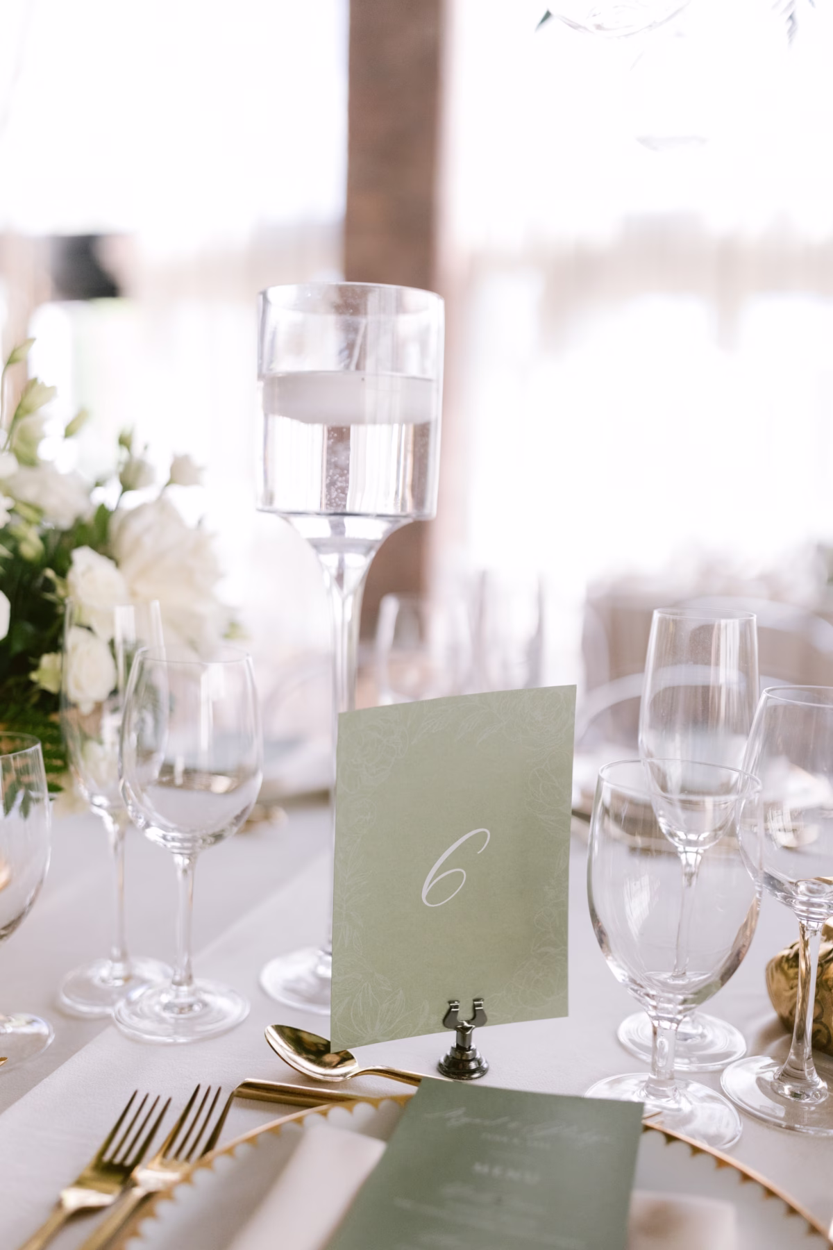 Elegant sage green table number 6 with gold flatware and white florals by Maky The Diva Flowers at The Roundhouse Beacon Hudson Valley wedding photographed by Ashley Izquierdo Photography