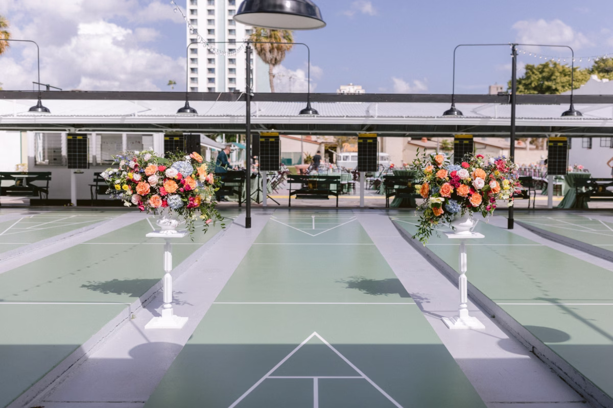 Colorful floral arrangements by Petite Fleur frame the shuffleboard court ceremony space at St Pete Shuffleboard Club wedding