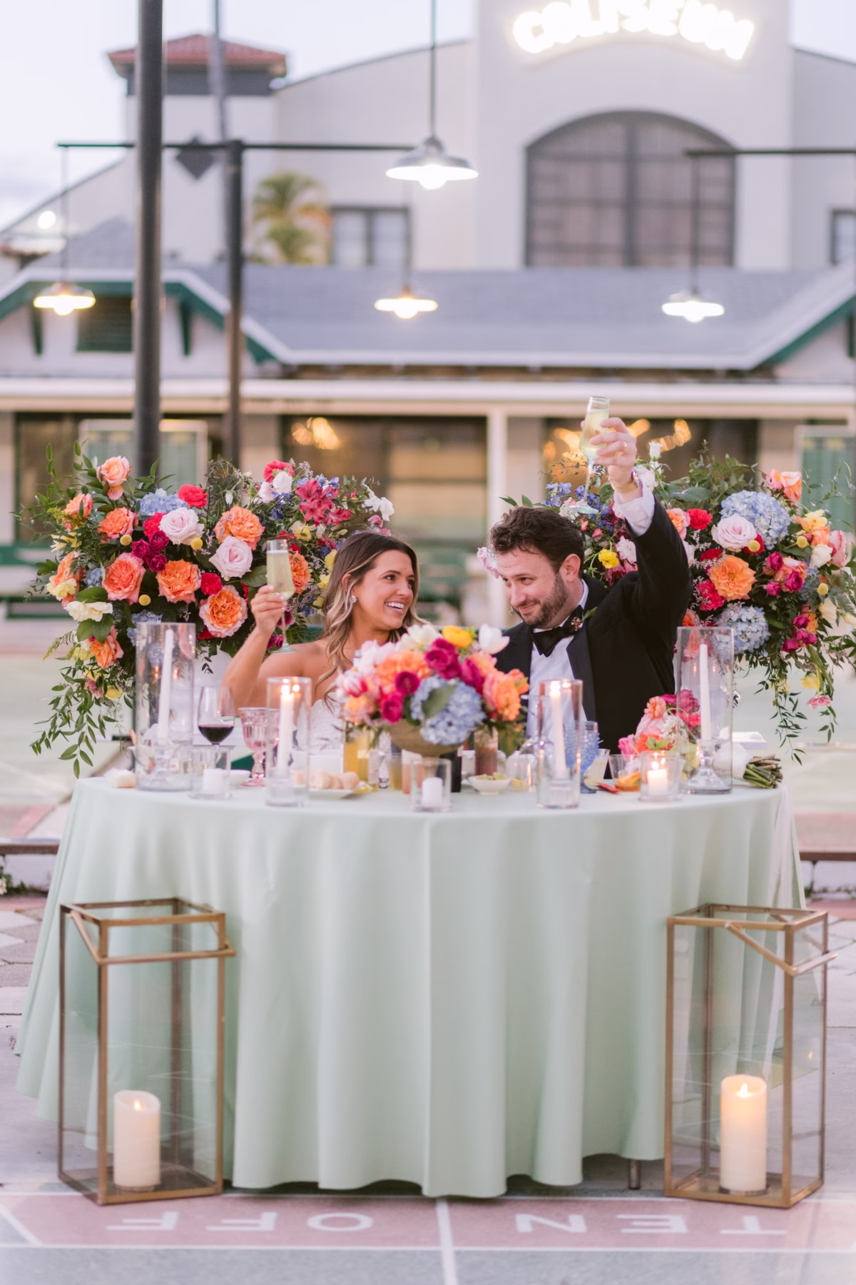 Bride and groom toasting at elegant sweetheart table with vibrant floral arrangements by Petite Fleur at St Pete Shuffleboard Club wedding coordinated by Day of Details