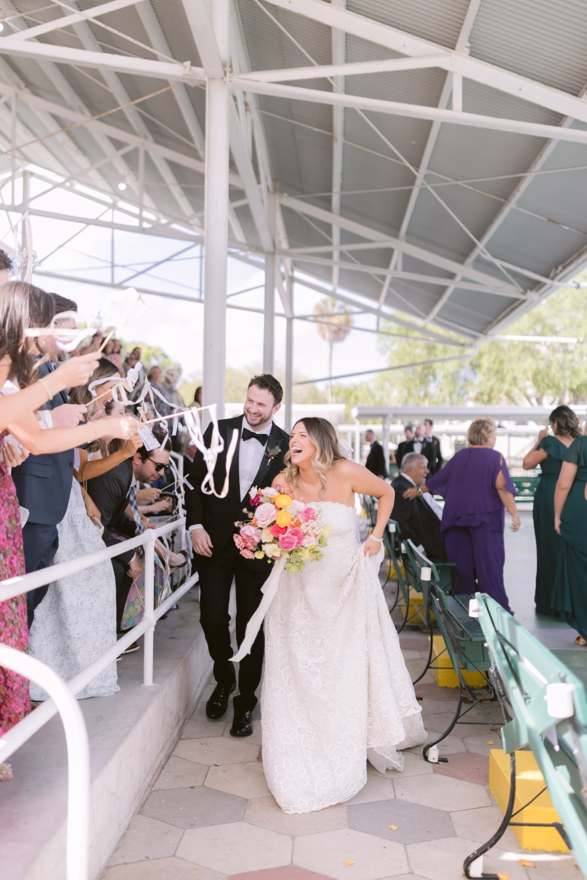Bride and groom exit through ribbon streamers at St Pete Shuffleboard Club wedding with colorful bouquet by Petite Fleur and coordination by Day of Details