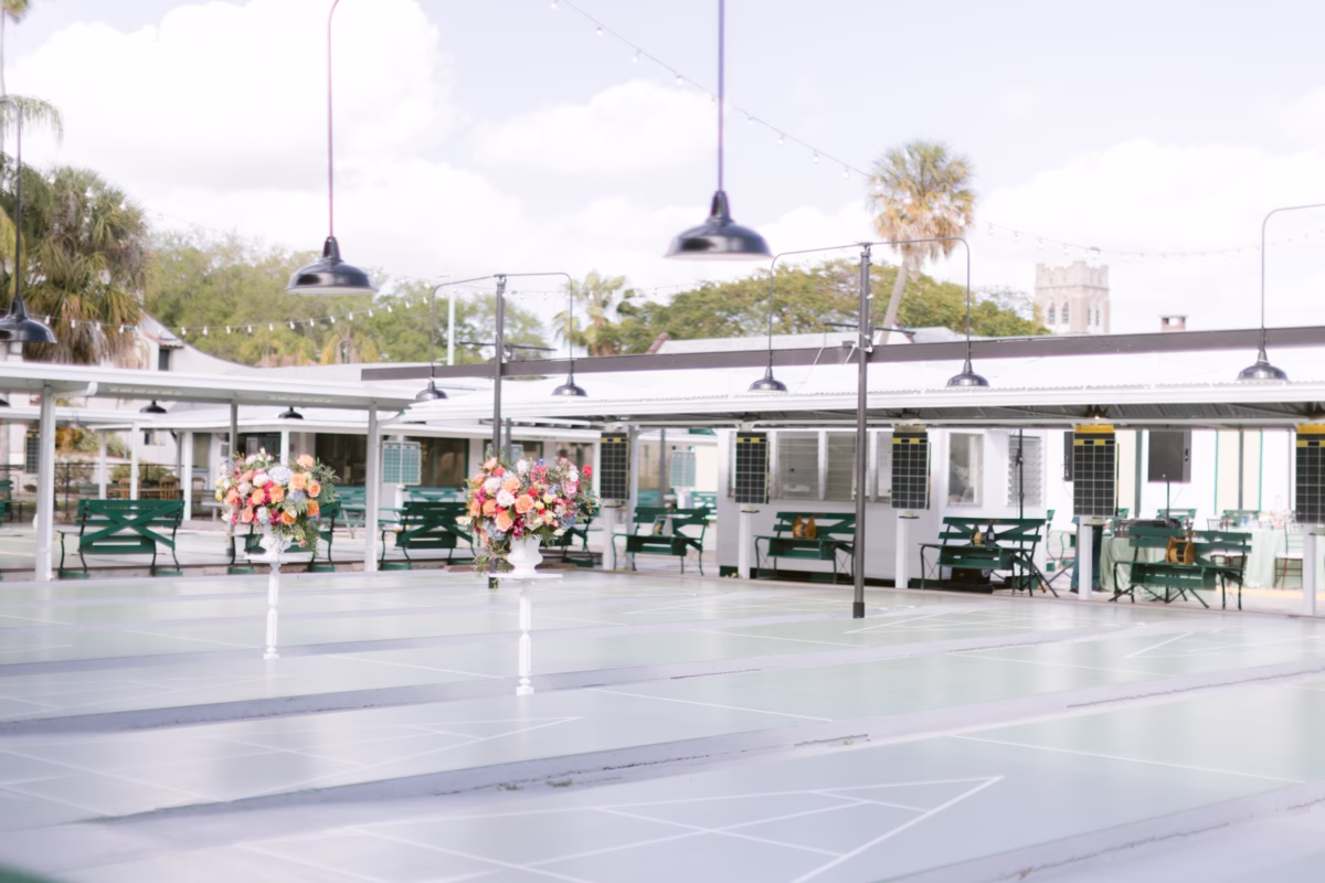 Wedding reception setup at St. Pete Shuffleboard Club with colorful floral centerpieces by Petite Fleur and green picnic tables coordinated by Day of Details