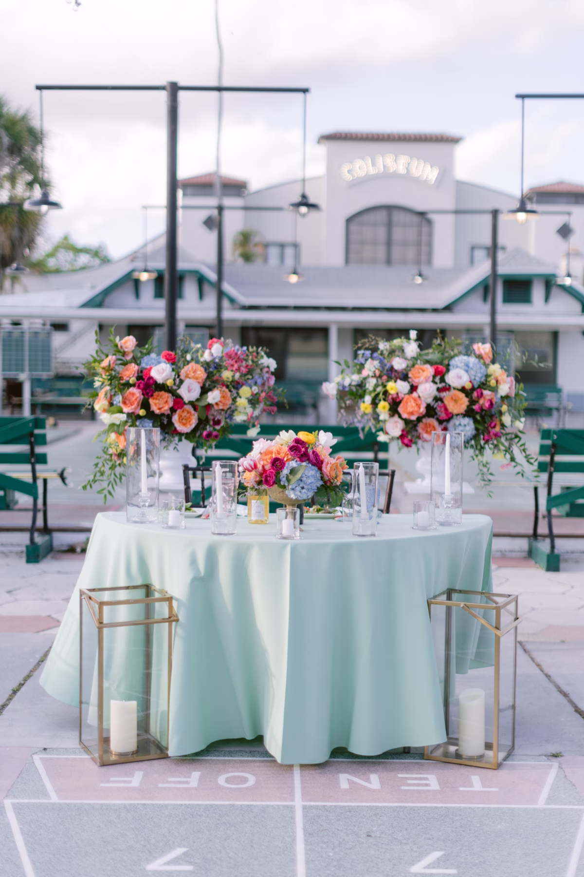 Elegant sweetheart table with colorful floral arrangements by Petite Fleur at St. Pete Shuffleboard Club wedding reception with gold geometric candle holders and mint linens