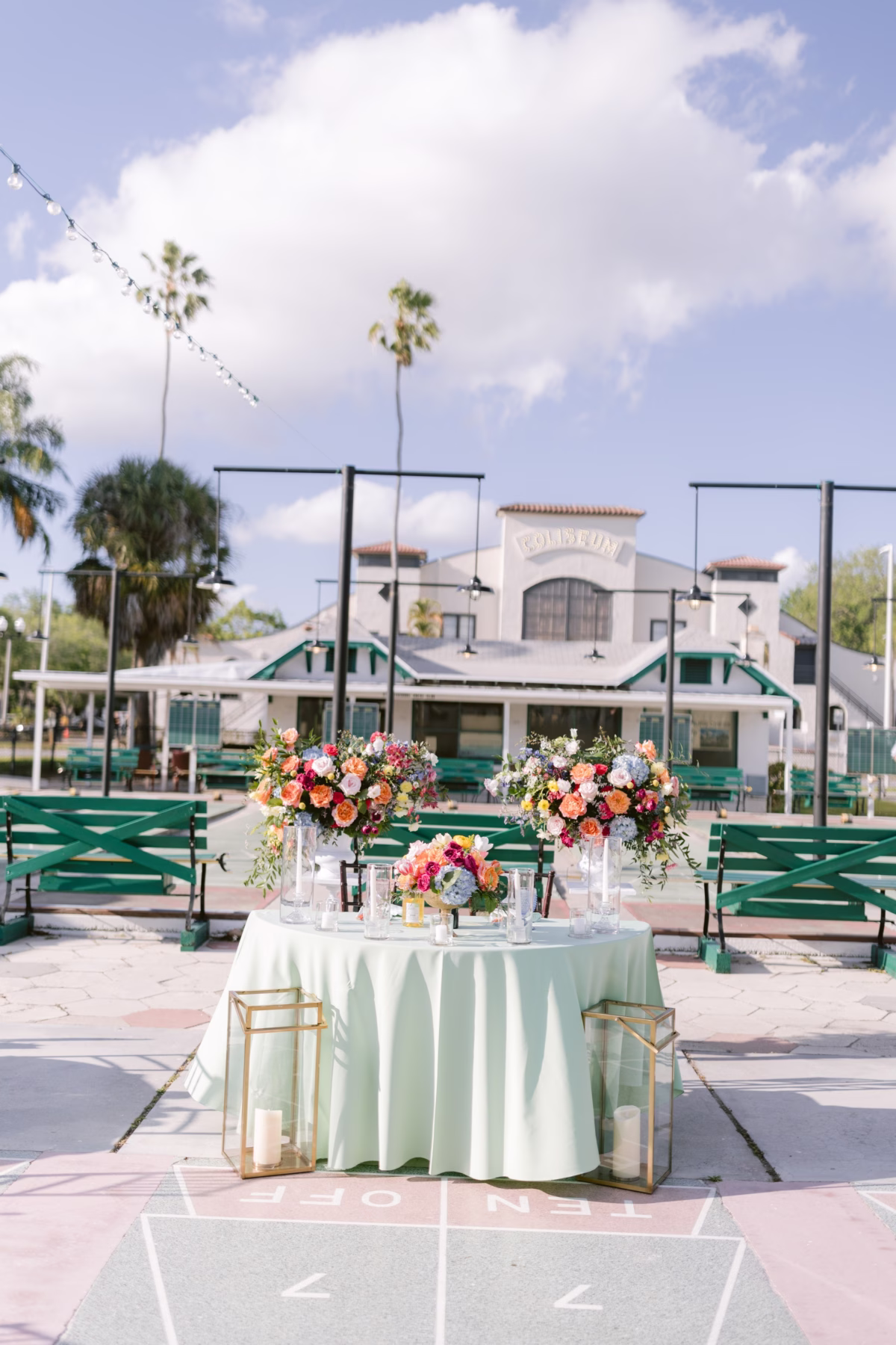 Elegant wedding reception table with colorful floral centerpieces by Petite Fleur at St. Pete Shuffleboard Club with green benches and historic venue backdrop