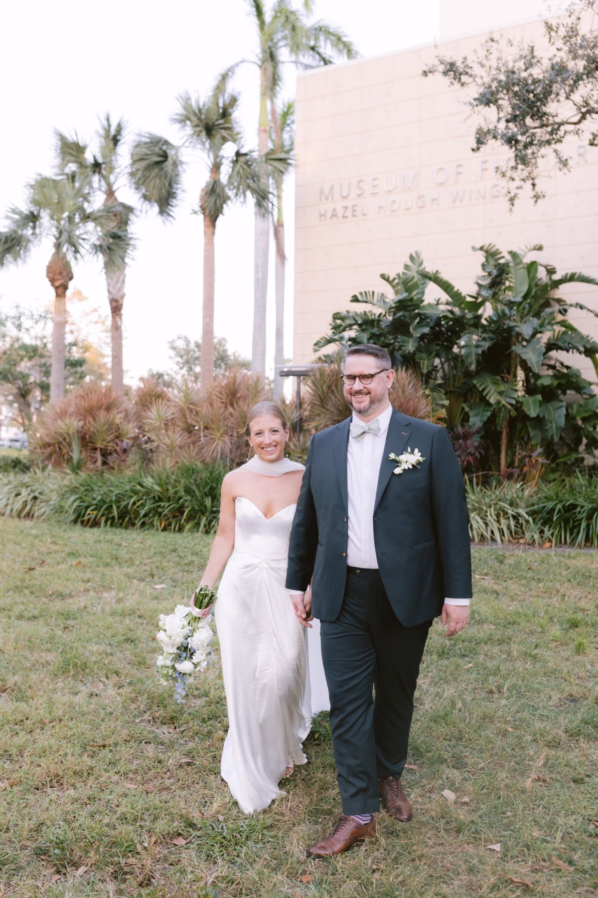 Bride and groom walking hand in hand with white wedding bouquet by Wonderland Floral Art at St. Petersburg art museum wedding photographed by Ashley Izquierdo Photography