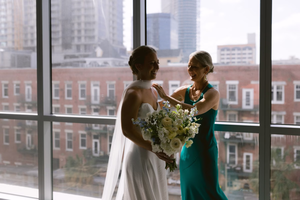 Bride holding white and green bouquet by Wonderland Floral Art while getting ready at Nancy Cotto Events venue in St. Petersburg with city skyline view