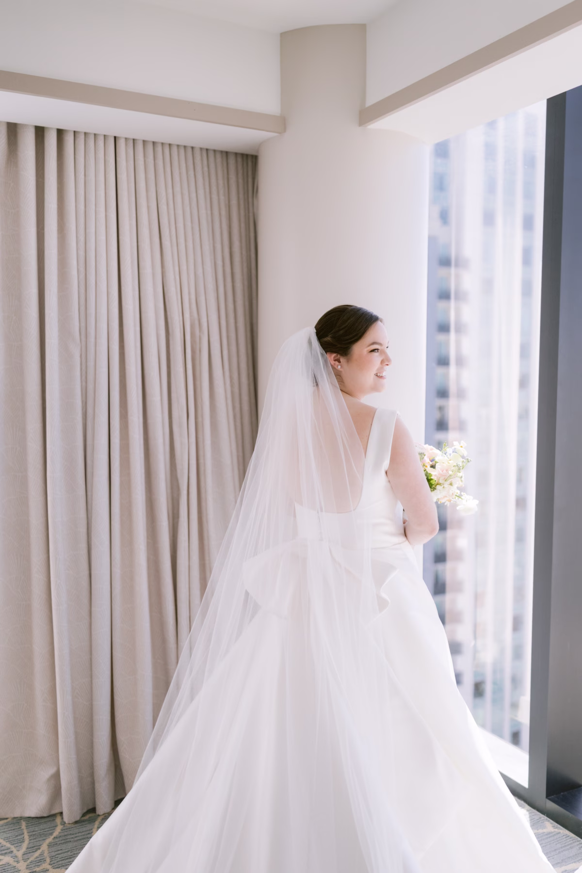 Bride in elegant wedding gown by The White Closet Bridal with white bouquet by I Dew Events during getting ready photos at JW Marriott Tampa Water Street photographed by Ashley Izquierdo Photography