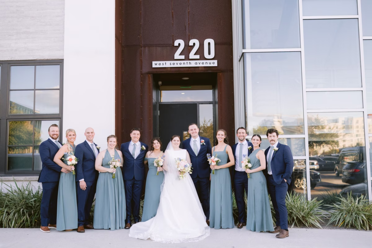 Wedding party portrait at Armature Works in Tampa featuring bride in white gown with bridesmaids in dusty blue dresses holding bouquets by I Dew Events florist