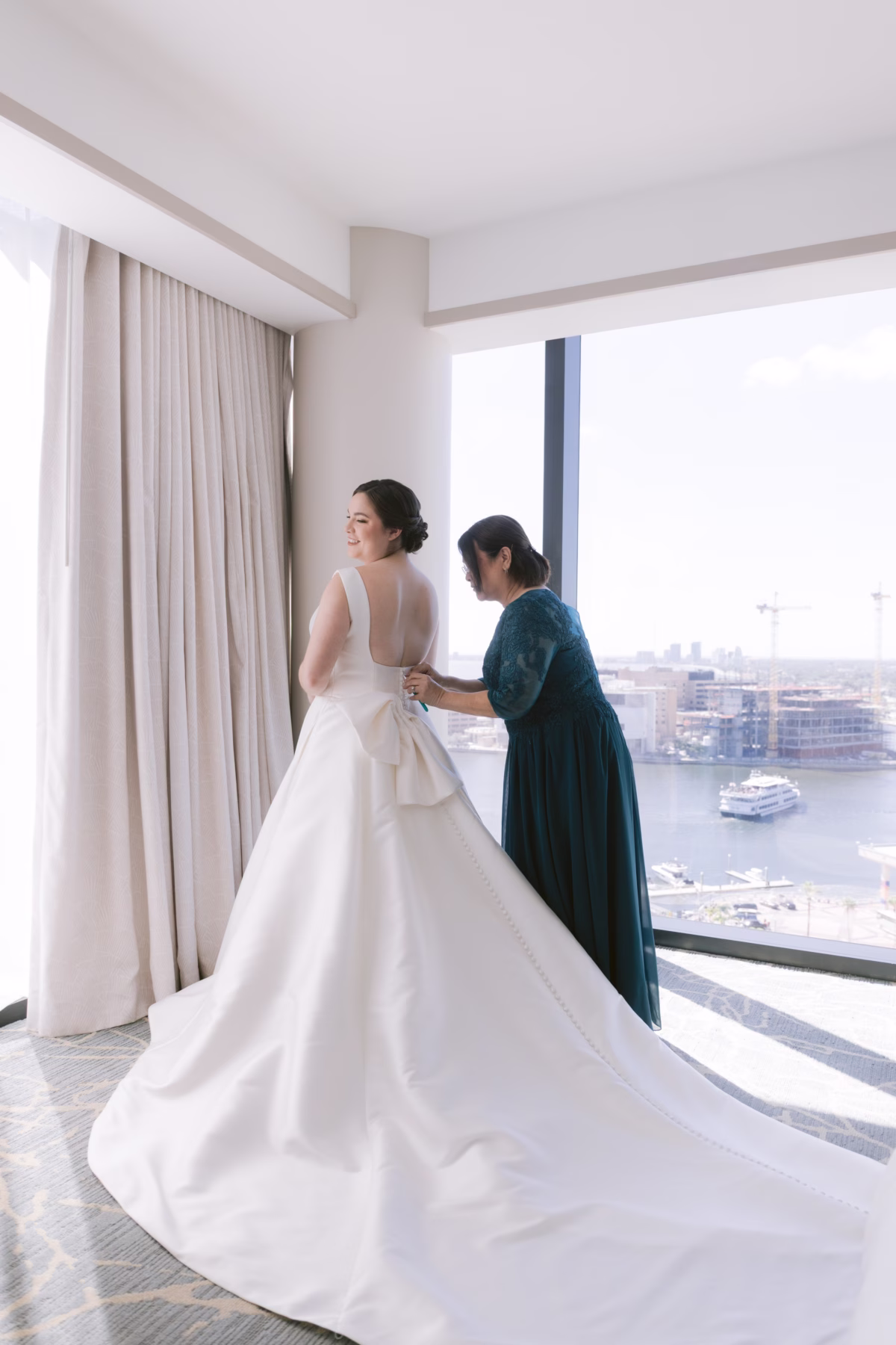Bride in elegant ballgown wedding dress from The White Closet Bridal getting ready at JW Marriott Tampa with mother helping with dress details