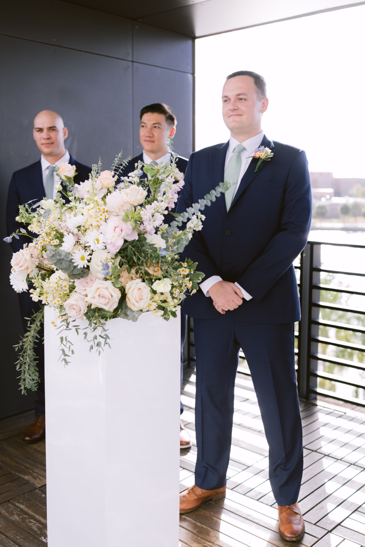 Groom and groomsmen waiting at ceremony with elegant white and blush floral arrangement by I Dew Events at Armature Works Tampa wedding
