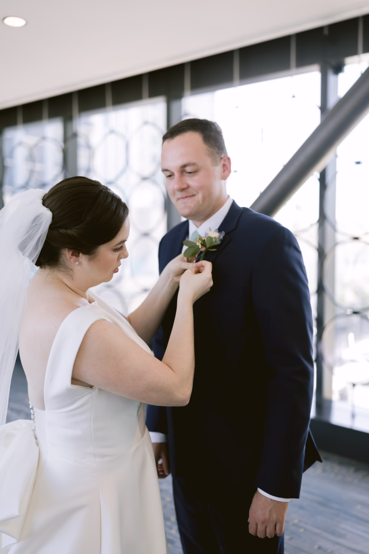 Bride adjusts groom's boutonniere by I Dew Events florist at Armature Works Tampa wedding photographed by Ashley Izquierdo Photography