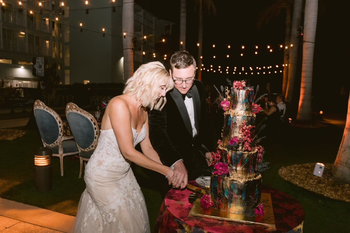 Bride and groom cutting their elegant dark wedding cake decorated with jewel-toned flowers at Casa Marina Key West reception