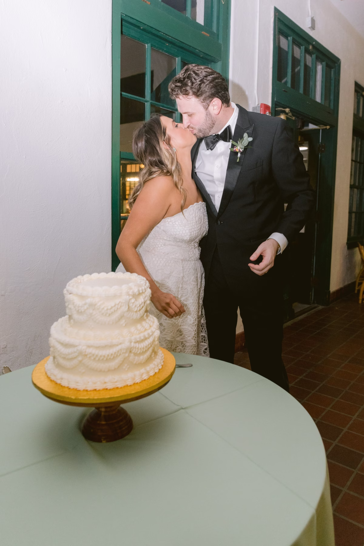 Bride and groom share a kiss during cake cutting with white tiered Publix wedding cake at St Pete Shuffleboard Club wedding