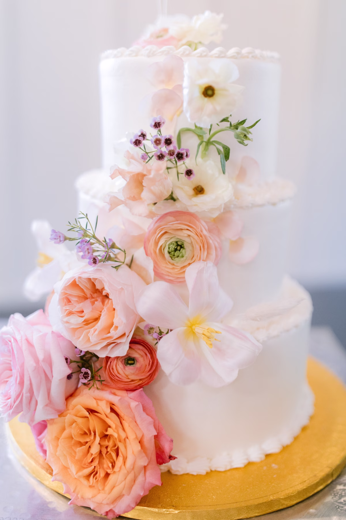 White tiered wedding cake decorated with coral and peach fresh flowers by Golden Wild Florals at Soire Estate Tampa garden wedding photographed by Ashley Izquierdo Photography