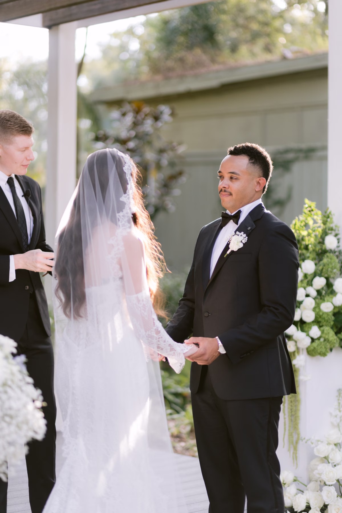 Outdoor wedding ceremony with white floral arrangements by Ava Elise Decor at Soire Estate Tampa featuring bride and groom exchanging vows