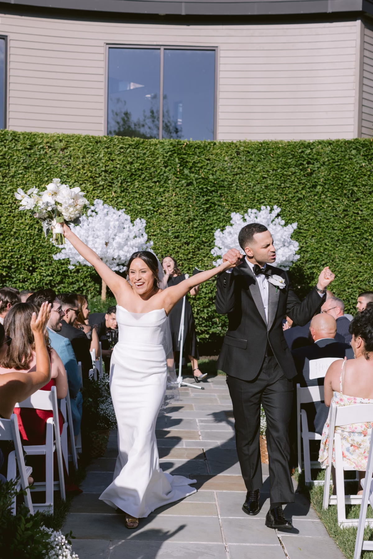 Newlyweds celebrate walking down the aisle after their wedding ceremony at The Roundhouse Beacon with white floral arrangements by Maky The Diva Flowers