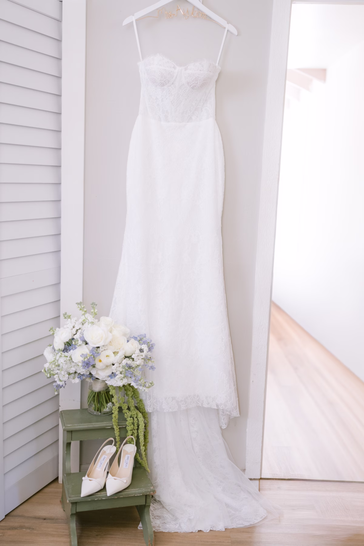 Elegant white wedding dress by Ella Blu Bridal hanging beside white and blue bridal bouquet by Ava Elise Decor at Soire Estate Tampa wedding