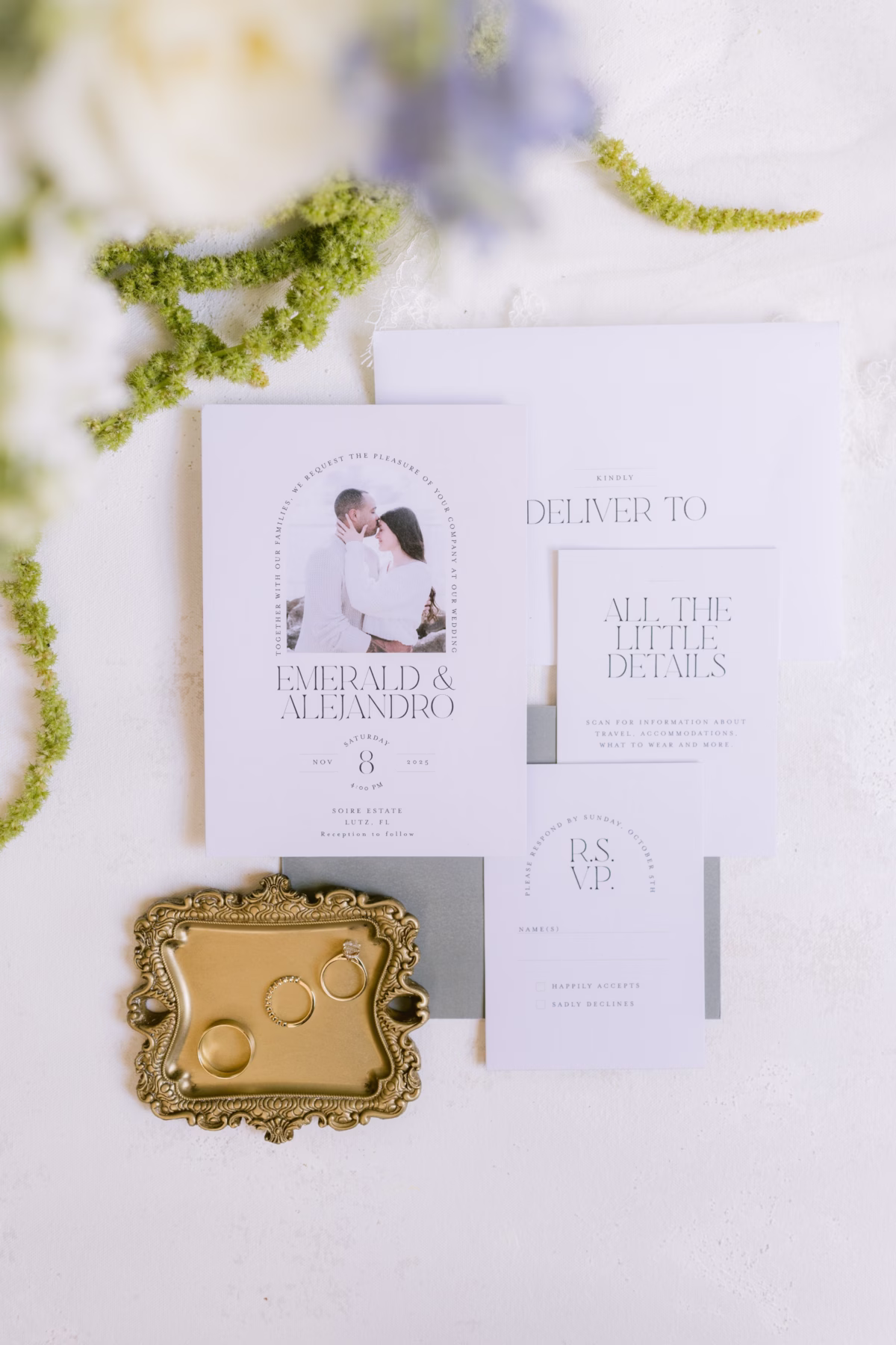 Elegant white wedding invitation suite with gold rings displayed on ornate tray with green florals for Tampa wedding at Soire Estate planned by Daniela Alvarez Event Planning