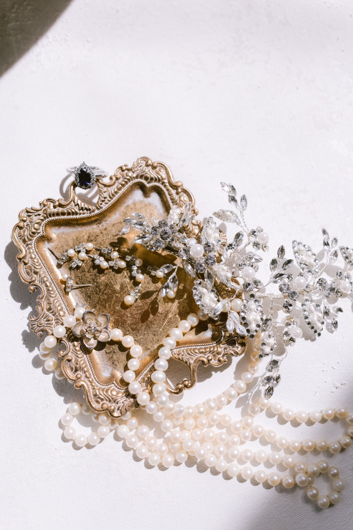 Elegant bridal jewelry details featuring pearl necklace and crystal headpiece on ornate gold tray at Armature Works Tampa wedding photographed by Ashley Izquierdo Photography