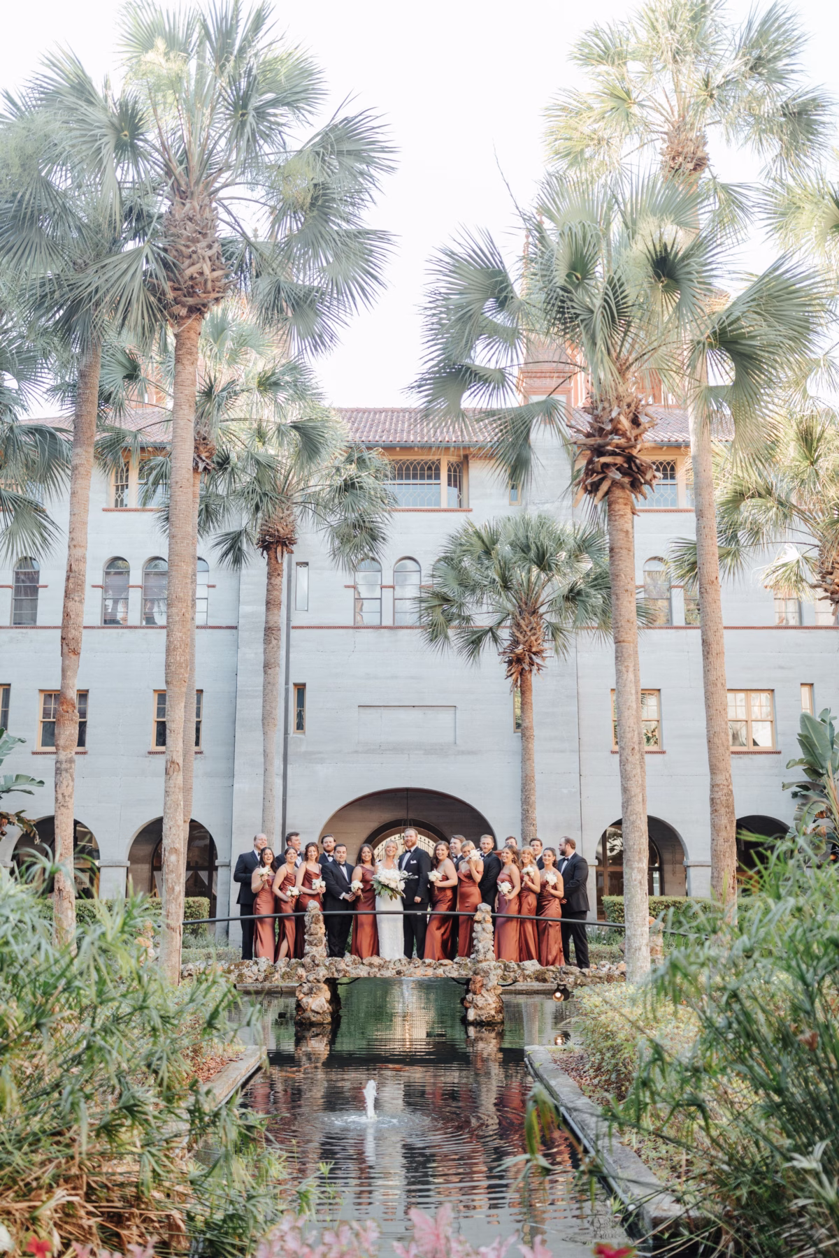Bridal party poses on stone bridge over reflecting pool at The Lightner Museum wedding planned by Coastal Celebrations in St. Augustine