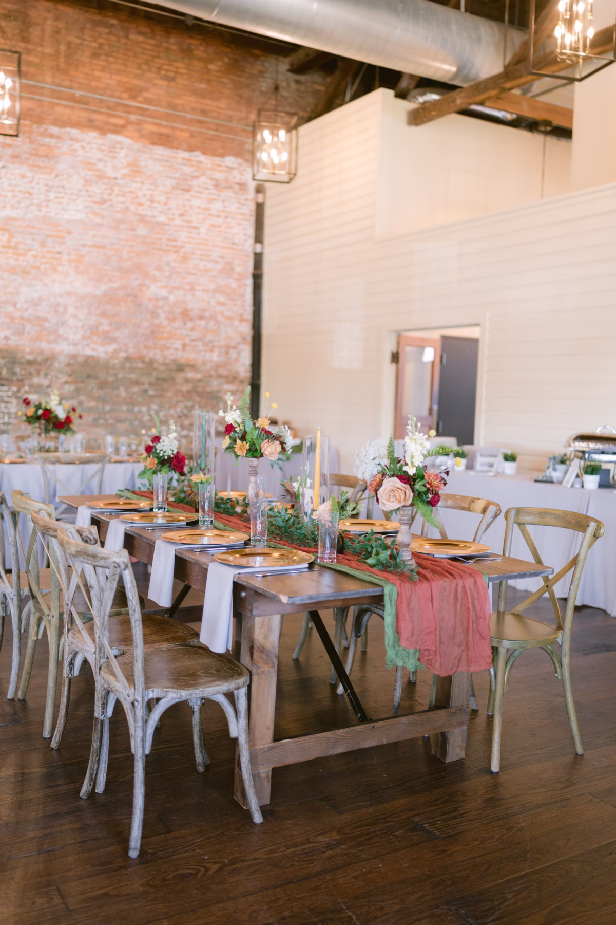 Rustic wedding reception tablescape with coral and peach floral centerpieces by Events in Bloom at Armature Works Tampa featuring exposed brick walls and cross-back chairs