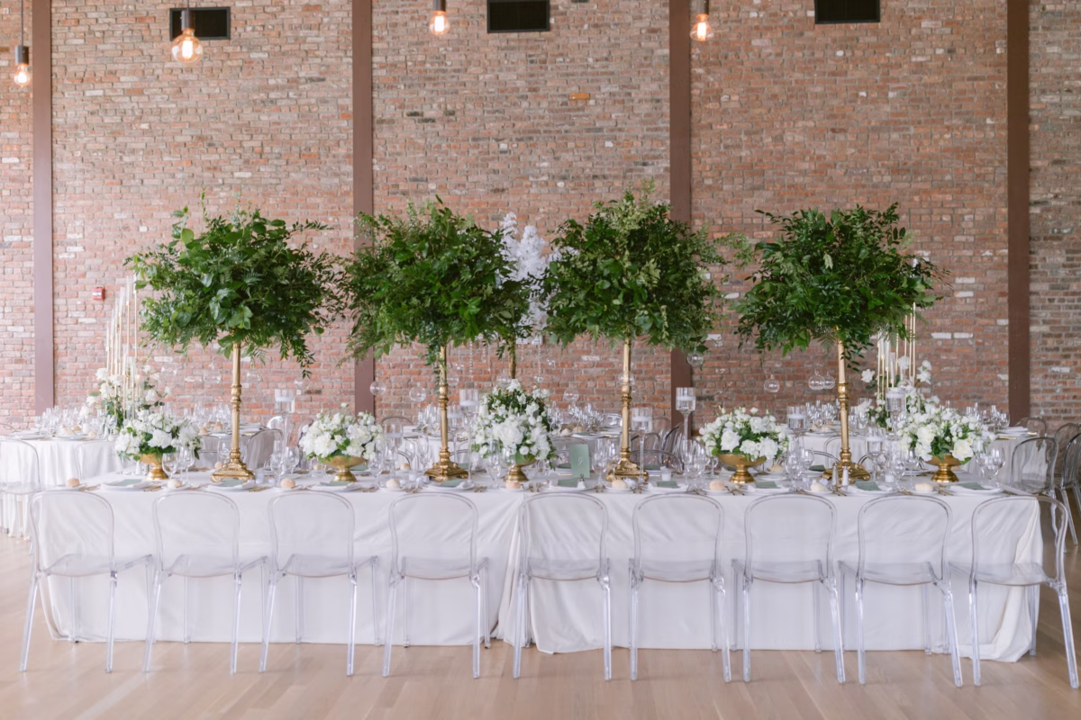 Elegant wedding reception tablescape with tall greenery centerpieces by Maky The Diva Flowers at The Roundhouse Beacon featuring exposed brick walls and clear ghost chairs
