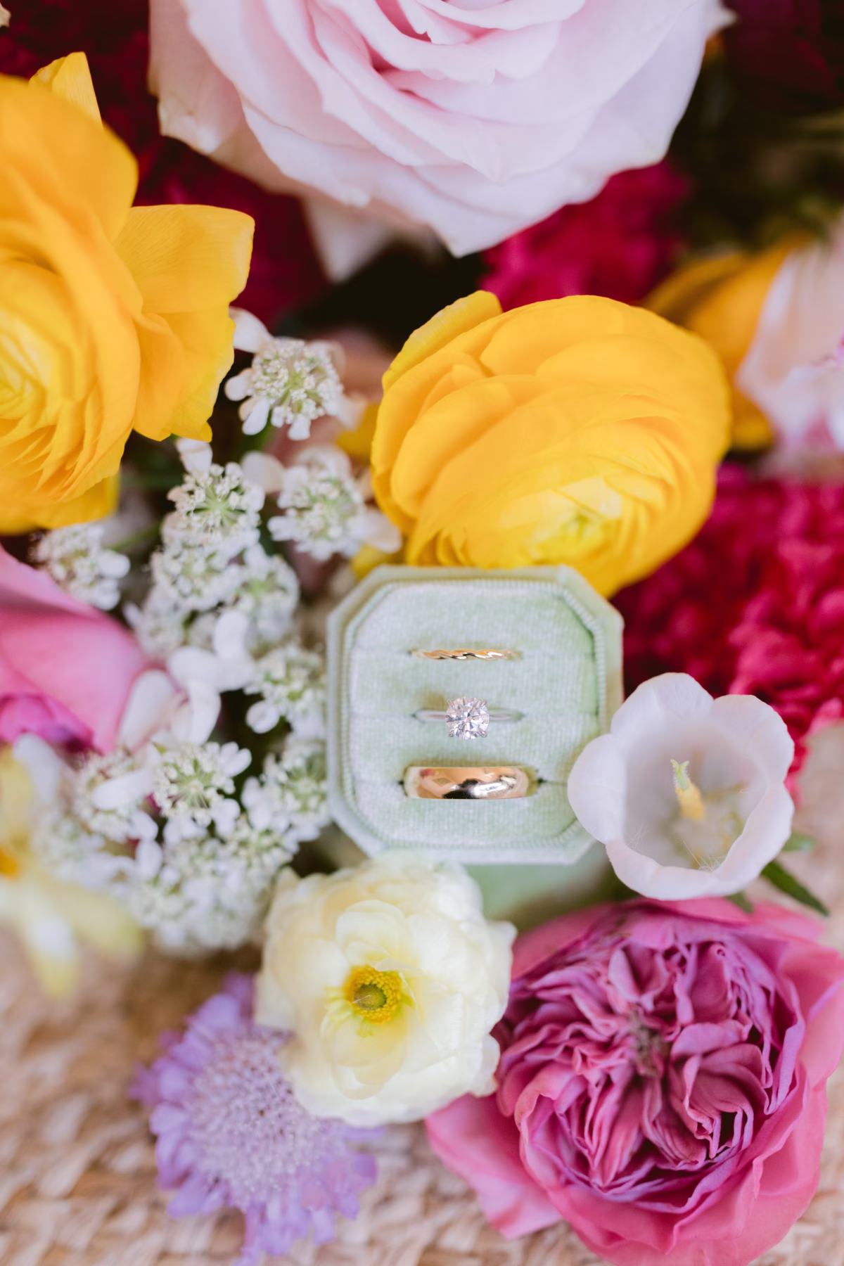 Wedding rings in mint green velvet box surrounded by vibrant yellow ranunculus and pink roses by Petite Fleur at St Pete Shuffleboard Club wedding
