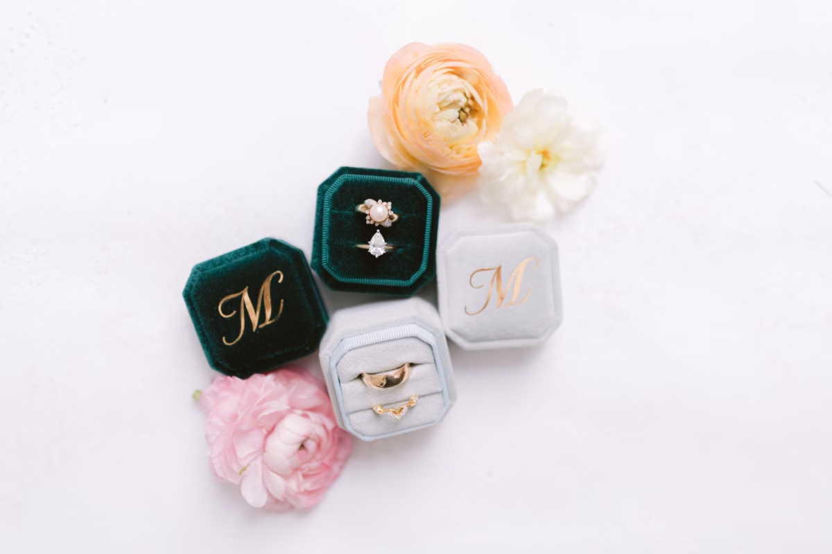 Elegant wedding rings displayed in velvet ring boxes with monogrammed stationery by Papier and ranunculus flowers at Soire Estate Tampa garden wedding