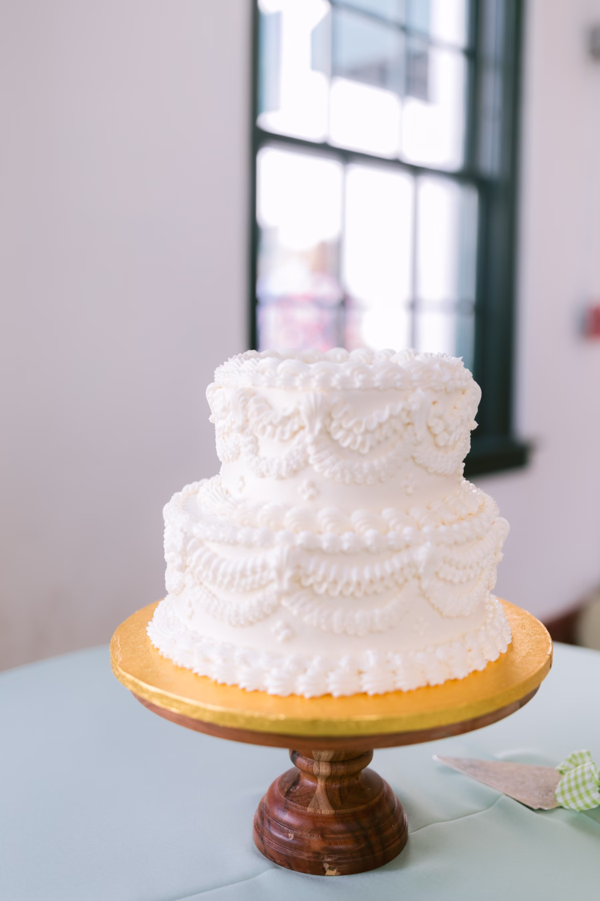 Elegant white pearl-detailed wedding cake by Publix displayed on gold cake stand at St. Pete Shuffleboard Club wedding venue