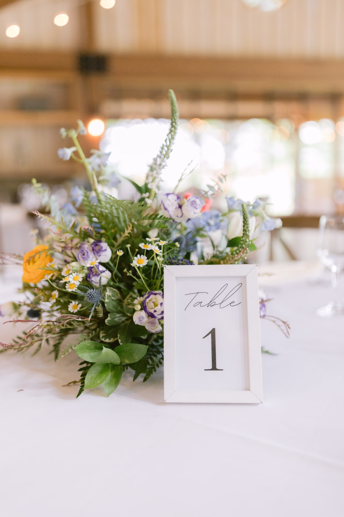 Wildflower centerpiece with purple blooms and ferns by Cherry Brandy Designs at Red Maple Vineyard wedding with table number one