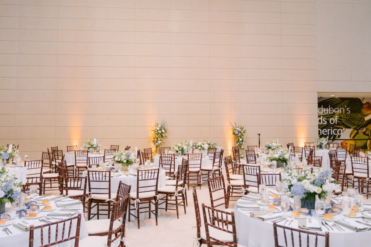 Elegant wedding reception with white floral centerpieces by Wonderland Floral Art at Nancy Cotto Events venue in St. Petersburg featuring gold chiavari chairs and uplighting